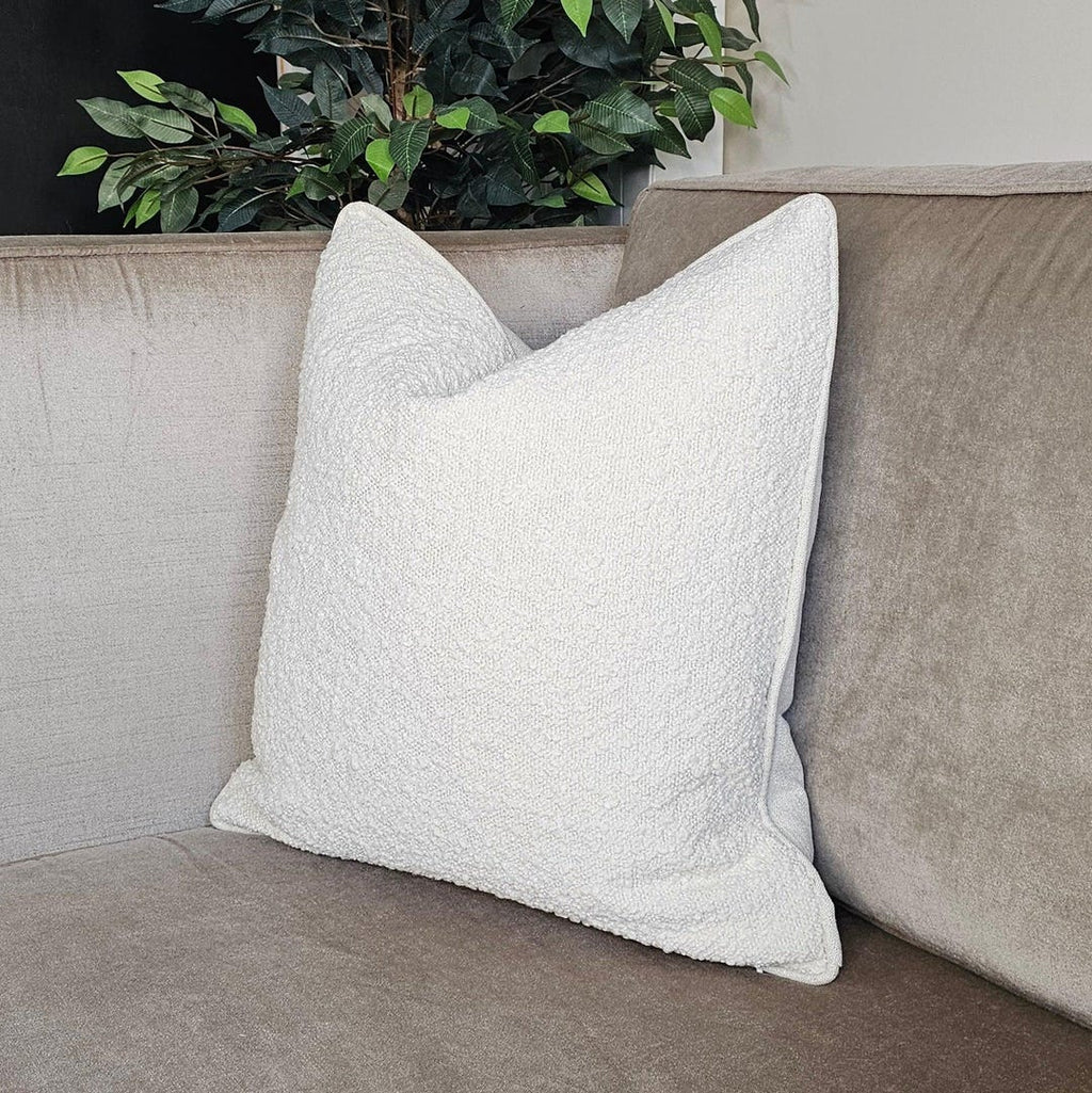 White textured throw pillow on beige luxury sofa with green plant background