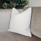 White textured throw pillow on beige luxury sofa with green plant background