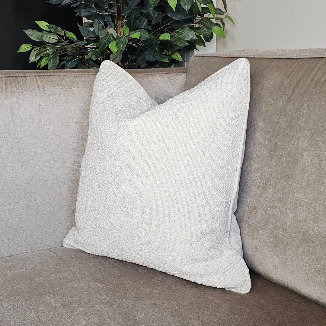 White textured throw pillow on beige luxury sofa with green plant background