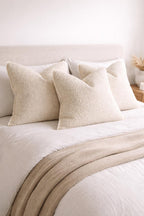 Luxury cream bouclé throw pillows on a cozy bed with neutral bedding and knit blanket