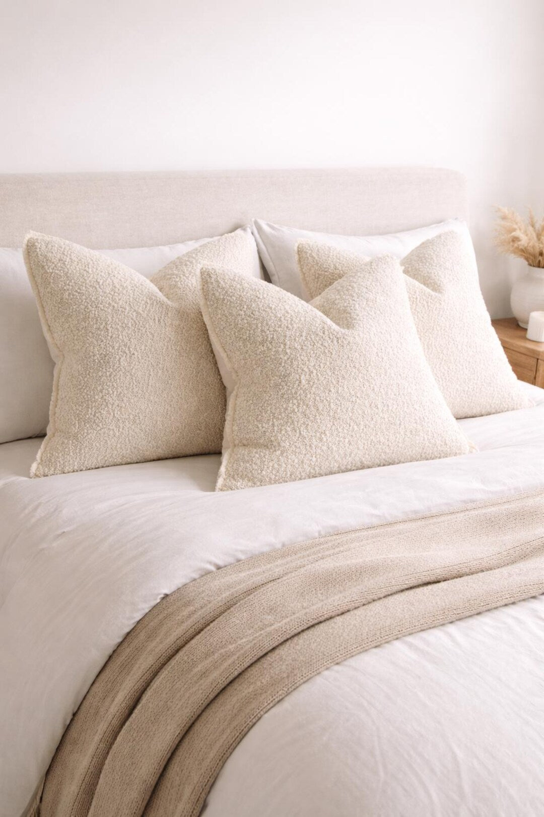 Luxury cream bouclé throw pillows on a cozy bed with neutral bedding and knit blanket