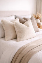 Luxury beige textured throw pillows on a cozy bed with neutral bedding and knit blanket