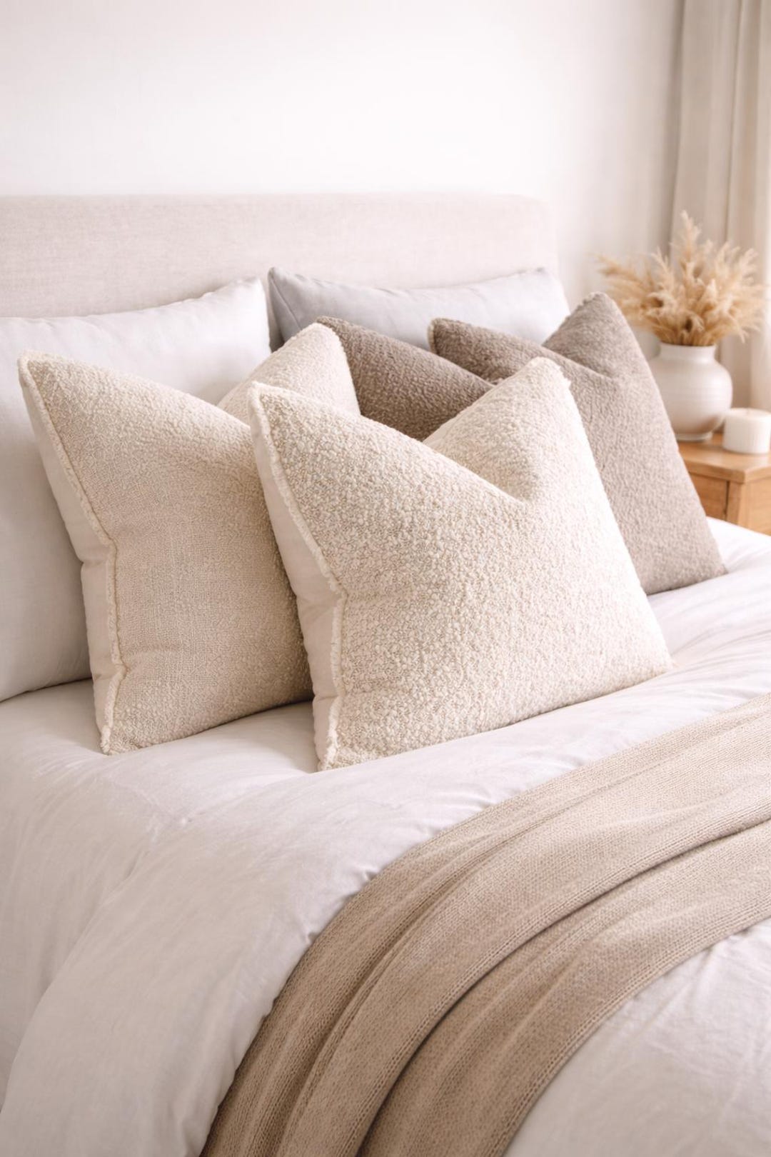 Luxury beige textured throw pillows on a cozy bed with neutral bedding and knit blanket