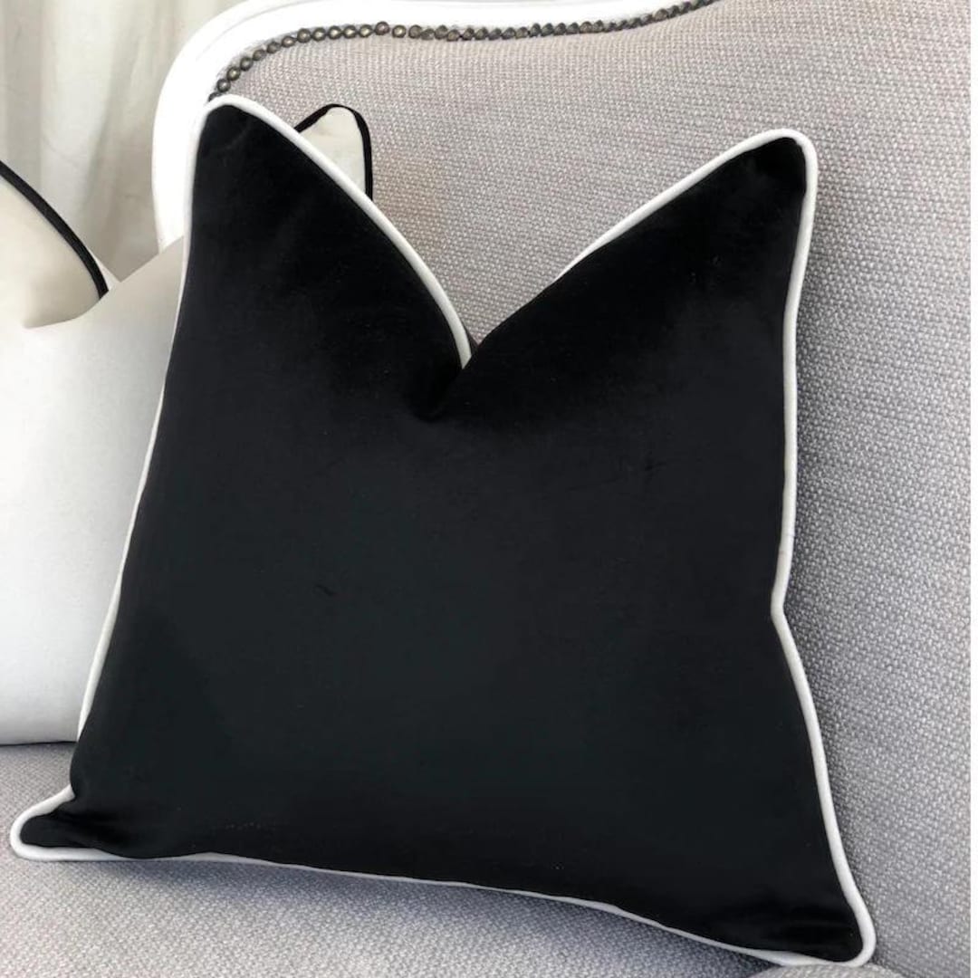 Black velvet throw pillow with white piping on grey sofa, luxury home decor accent