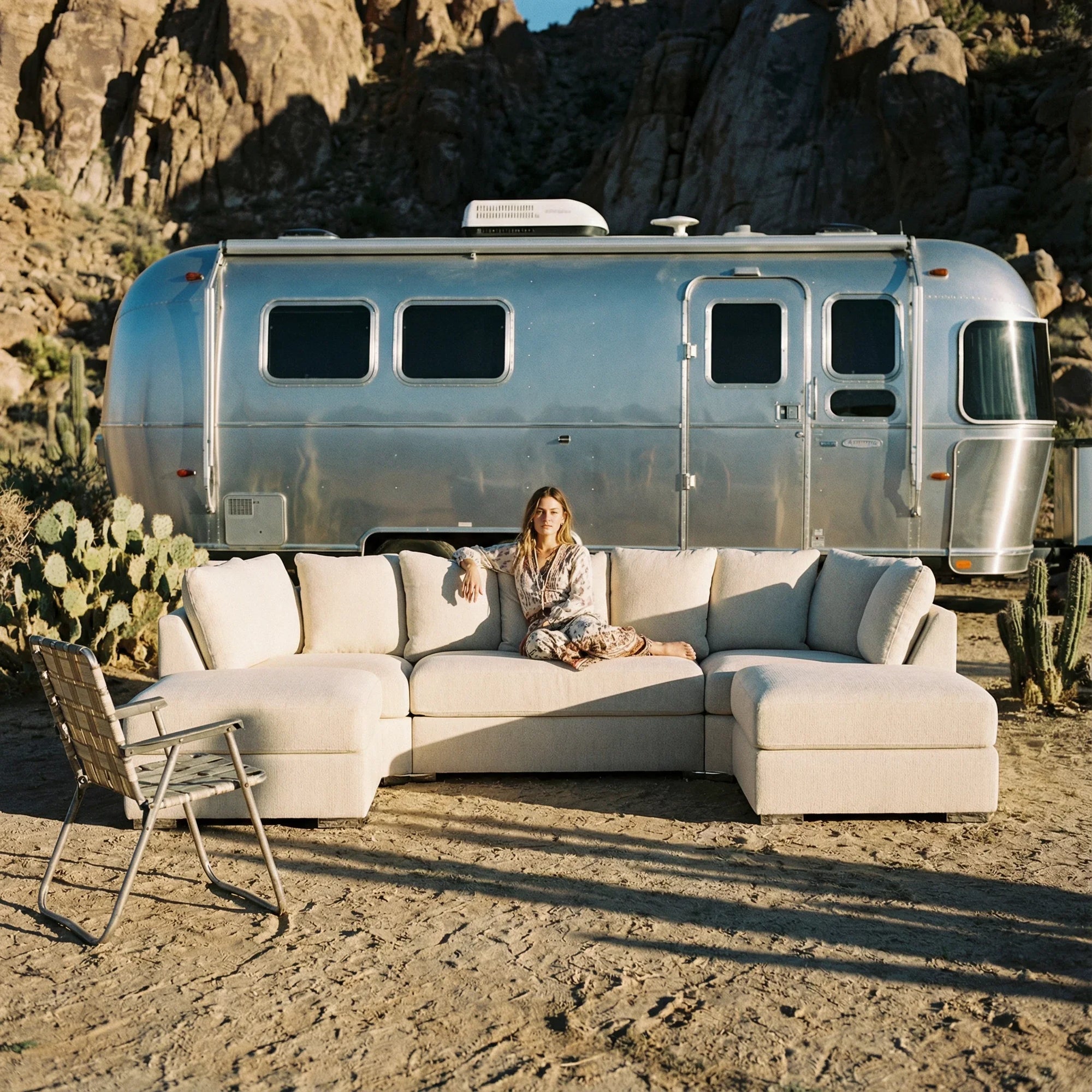 Modern cream sectional sofa outdoors with woman seated, Airstream trailer and desert backdrop