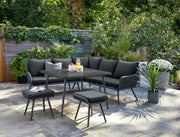 Modern black outdoor sofa set with dining table and stools on patio, surrounded by greenery