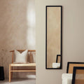 Tall black-framed wall mirror in modern living room with wooden bench and neutral decor