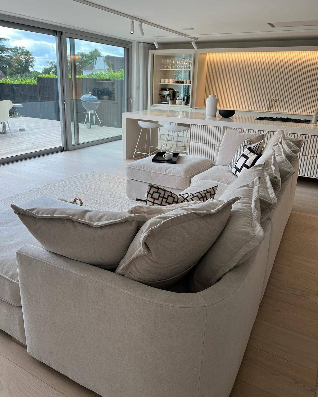 Modern open-plan living room with light grey U-shaped sofa, kitchen island, and large windows.