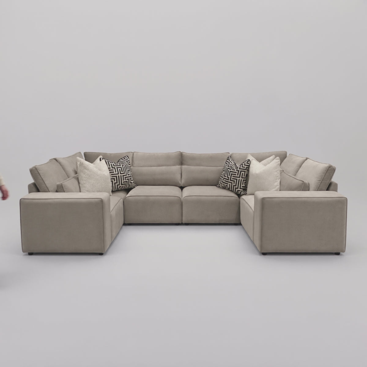 Maison Closed-End U-Shape Sofa in a minimal studio with an adult model demonstrating scale