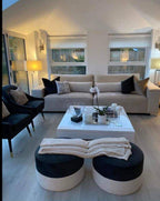 Modern living room with beige 4-seater sofa, footstools, black accent chairs, and coffee table