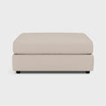 Modern beige fabric footstool ottoman with low black legs on a plain background