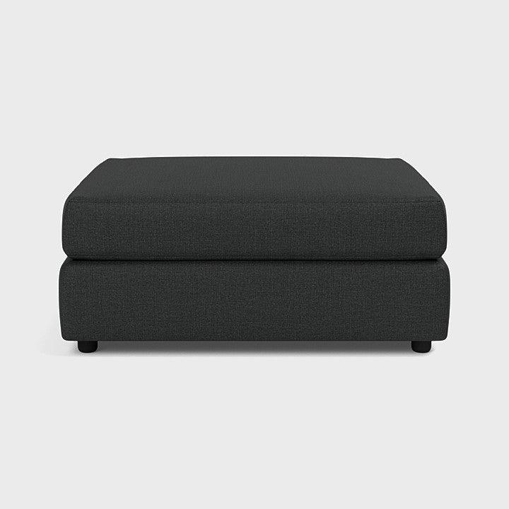 Modern dark grey footstool ottoman with fabric upholstery on a light background