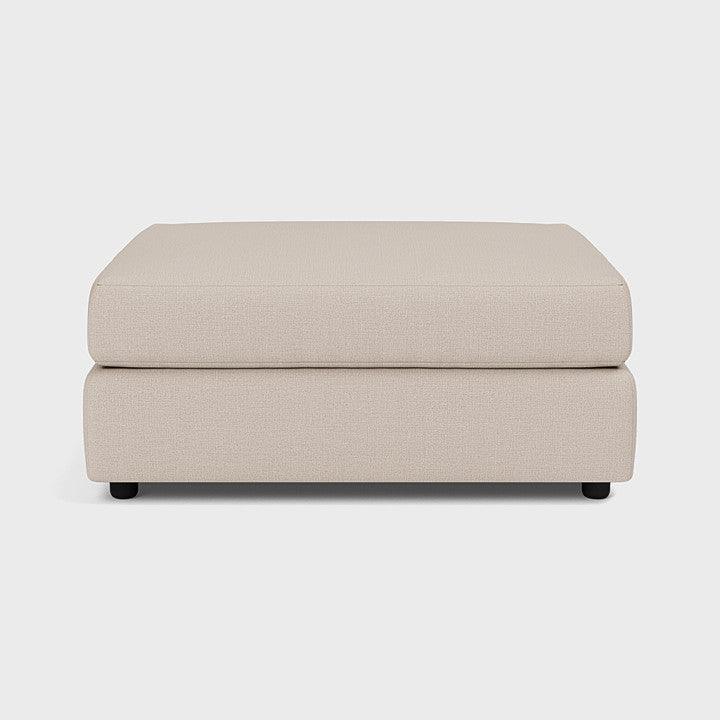 Modern beige upholstered footstool with clean lines on a plain background