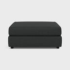 Modern dark grey fabric footstool ottoman with clean lines on a light background
