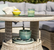 Outdoor wicker table with bowls, plates, and drink, set beside grey patio sofa for garden dining